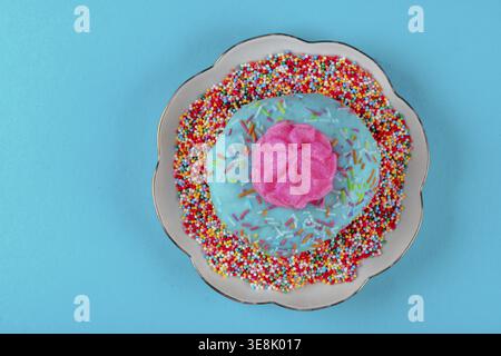 Auf dem Teller ist ein rosafarbener Kuchen mit mehrfarbigen Streuseln. Die Platte ist auf blauem Hintergrund Stockfoto