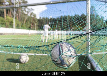 Der Fußball liegt im Netz auf dem Spielfeld mit unscharfen Spielern im Hintergrund. Fußball ist ein Sport. Das Konzept, ein Ziel zu erreichen Stockfoto