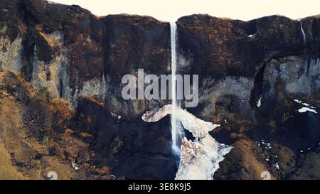 Blick aus der Vogelperspektive auf foss, eine Sidu-Kaskade in island, die von Hügeln abfließt und eine skandinavische Landschaft bildet. Wunderschöner isländischer Wasserfall, der über verschneite Berge fließt. Zeitlupe. Stockfoto
