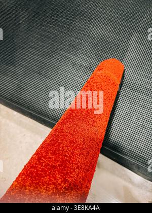 Makroansicht einer hellroten Malerwalze mit strukturiertem Nickerchen auf einer dunklen Gummioberfläche. Ideal für Renovierungskonzepte, Heimwerkereinrichtungen, Heimwerkereinrichtungen Stockfoto