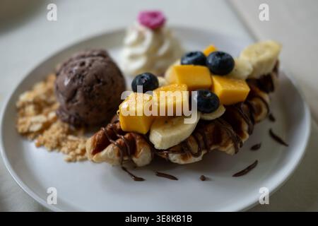 Waffel mit Schokoladeneis serviert mit Bananenscheiben und Mango, Schlagsahne und Sauce. Stockfoto