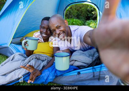 Vertikales Video: Afroamerikaner Vater und Sohn in blauem Zelt mit Tassen, Vater macht Selfie, um sich zu erinnern Stockfoto