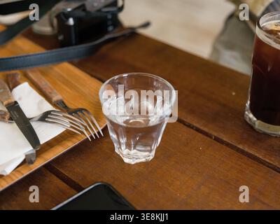 Ein klares Glas Trinkwasser in der Nähe des hölzernen Kaffeetisches. Dieses Bild zeigt ein Glas Wasser, Nahaufnahme, Hintergrundunschärfe. Ein einfacher Glasbecher von Ccle Stockfoto