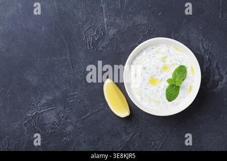 Tzatziki-Dip-Sauce oder Dressing aus griechischem Joghurt, dekoriert mit Zitrone und Minze. Traditionelle mediterrane Küche. Draufsicht Stockfoto