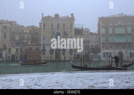 Canal Grande in Venedig an einem nebeligen Wintertag. Gondoliere, der an einer Gondel mit einem Motorboot auf dem Canal Grande vorbeifährt. Stockfoto