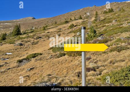 Leeres gelbes Pfeilschild, das in Richtung auf Berghang zeigt. Platz für Text auf dem leeren Wegweiser. Stockfoto