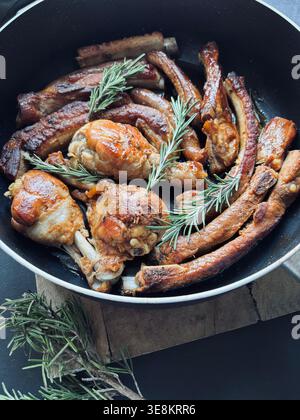 Gebratenes gemischtes Fleisch mit Hähnchenstangen und Schweinerippchen, gewürzt mit frischem Rosmarin. Traditioneller, rustikaler italienischer „gemischter Grill“ in einer Pfanne gekocht. Stockfoto