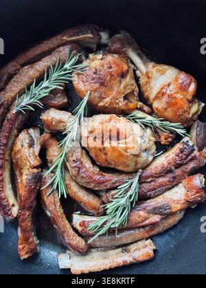 Gebratenes gemischtes Fleisch mit Hähnchenstangen und Schweinerippchen, gewürzt mit frischem Rosmarin. Traditioneller, rustikaler italienischer „gemischter Grill“ in einer Pfanne gekocht. Stockfoto