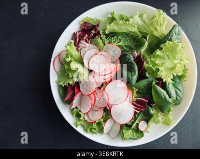 Frischer gemischter Salat mit Radieschen, serviert in einer weißen Schüssel, dunkler Hintergrund. Gesunde Ernährung, mediterrane Ernährung, frisches saisonales Zutatenkonzept. Stockfoto
