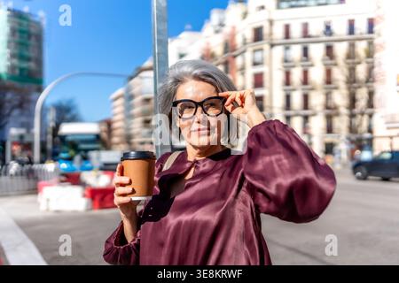 Reife Frau genießt Kaffee, während sie in der Stadt spaziert Stockfoto