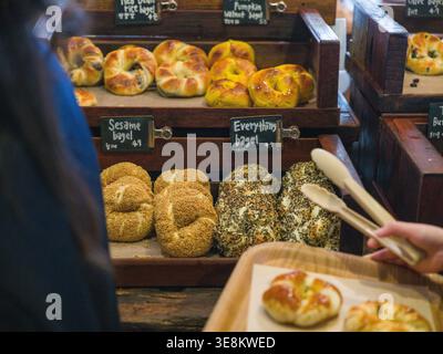 Weitwinkelhandwerkliche Bäckerei Innenausstattung Bagel-Vielfalt auf Holztabletts. Dieses Bild zeigt ein breites Display für Bäckerei, Bagel-Vielfalt, Tabletts und Schwarze Bretter. Insid Stockfoto
