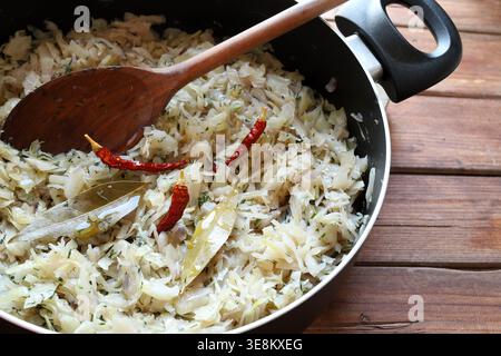 Traditionelles hausgemachtes Sauerkraut mit Lorbeerblättern und roten Chilischoten in einer schwarzen Pfanne auf einem Holztisch. Draufsicht. Stockfoto