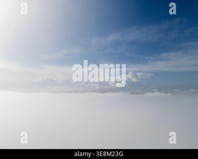 Luftaufnahme über dicken Wolken mit Sonne, die durch den Horizont blickt Stockfoto