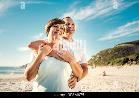Liebe, paarweise und glücklich mit Sightseeing am Strand für einen Jubiläumsausflug, eine Verbindung oder Urlaub. Umarmen, reife Leute und Lächeln mit Blick auf das Meer Stockfoto