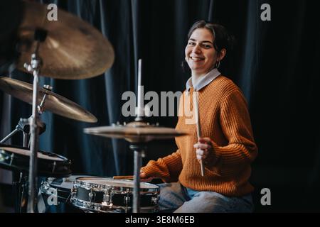 Eine junge Schlagzeugerin spielt Schlagzeug in einem Studio, lächelt beim Üben an einem Schlagzeug Stockfoto