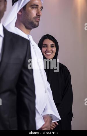 Emirati-Business-Team mit lächelnder Frau in Abaya, die hinter Kollegen bei einer Firmenveranstaltung steht Stockfoto