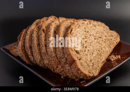 Helles Roggenbrotbrot, aufgefächert auf dunkler quadratischer Keramikschale. Poröse Krume und rustikale, verkleierte Kruste vor dunklem Hintergrund. Stockfoto