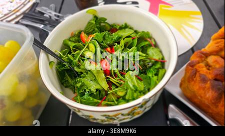 Speisen im Freien mit einem hausgemachten Gartensalat mit Blattgemüse, Tomaten und Gurken auf einem Holztisch. Stockfoto