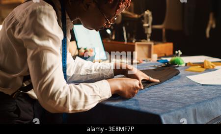 Maßgeschneidertes Messen von Gewebe in der Werkstatt, Überprüfung von Materialmaße, maßgeschneiderte Bekleidungslinie. Mitarbeiter, der an der Luxusmode-Kollektion im Modeatelier arbeitet. Handgeführte Aufnahme. Nahaufnahme. Stockfoto
