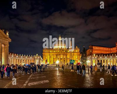 Leute, die am Abend in der Vatikanstadt durch den Petersplatz vor einem beleuchteten Petersdom spazieren Stockfoto