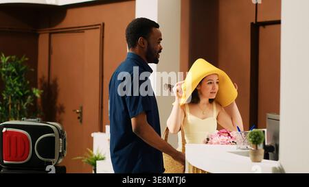 Ein junges Paar an der Hotelrezeption kam zum Einchecken, im tropischen Sommerresort. Verschiedene Gäste, die sich in der Empfangshalle anmelden, Trolley-Taschen mitnehmen und auf Urlaubsreise reisen. Stockfoto