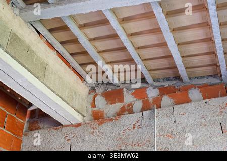 Nahaufnahme der unfertigen Innenwände aus roten Ziegeln und Betonbalken, die eine Deckenkonstruktion stützen Stockfoto