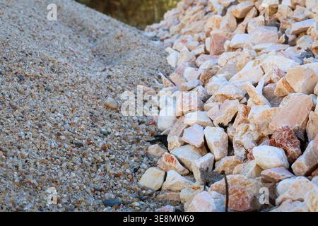 Eine detaillierte Textur, die den Kontrast zwischen feinem körnigem Sand und rauen, eckigen Steinen zeigt, was auf eine Konstruktion oder eine natürliche Landschaft hindeutet Stockfoto