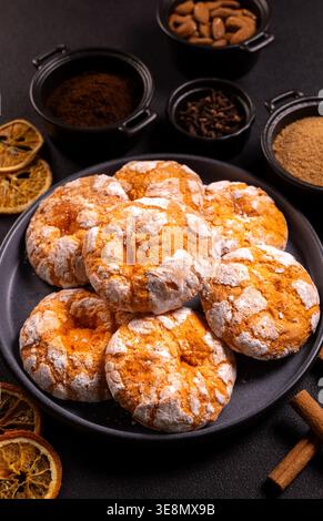 Teller mit hausgemachten Knitterkeksen, umhüllt von Kaffeeschalen, Nelken, braunem Zucker, Mandeln und getrockneten Orangenscheiben auf A Stockfoto