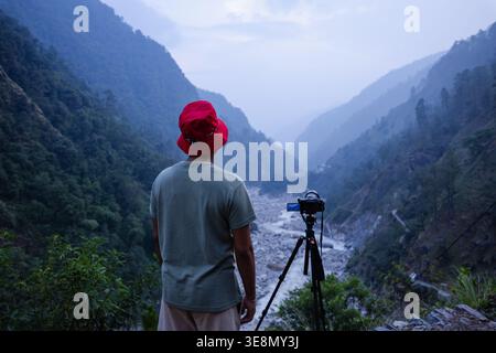 Ein Fotograf stellt seine Kamera auf, um die atemberaubende Landschaft des Madhyamaheshwar Tempels in Uttarakhand, Indien, zu erfassen, umgeben von majestätischen Bergen, Stockfoto