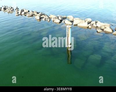 Die Pier-Unterstützung spiegelt sich in klarem Ostseewasser bei Sellin auf der Insel Rügen mit eingetauchten Granitbruchsteinen wider. Kopierraum. Stockfoto