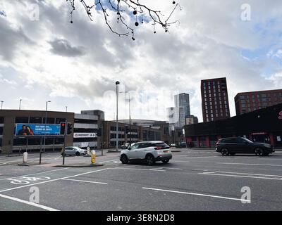 Manchester, Großbritannien - 22. Februar 2026: Geschäftige Kreuzung mit Autos, moderne Hochhäuser und dramatischer bewölkter Himmel in Manchester UK. Stockfoto