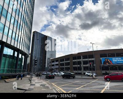 Manchester, Großbritannien - 22. Februar 2026: Belebte Stadtstraße mit Glasbüros, Parkhaus, Verkehr und Fußgängern in Manchester, Großbritannien. Stockfoto