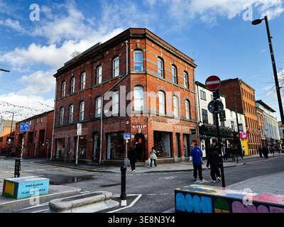 Manchester, Großbritannien - 22. Februar 2026: Historisches Eckgebäude aus rotem Backstein und Straßenszene in Manchester, Großbritannien, mit Einkaufsmöglichkeiten und Stadtatmosphäre. Stockfoto
