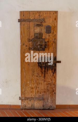 Eine verwitterte, schwere Holztür mit komplizierten, rostigen Metallschlössern und Scharnieren, die auf einen historischen oder sicheren Ort hinweisen Stockfoto
