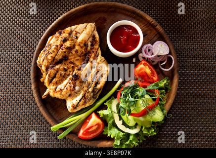 Gegrilltes Hühnersteak mit Gemüse und Ketchup, Nahaufnahme. Gebratenes Steak mit Salatgerichten. Draufsicht. Stockfoto