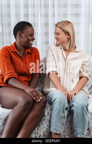 Zwei junge Frauen, die lächeln und reden, sitzen auf einem Sofa Stockfoto