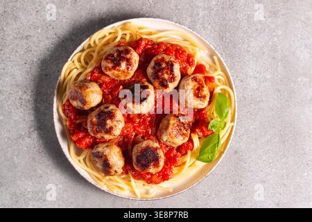 Ein Teller mit klassischen Spaghetti, garniert mit gebräunten Fleischbällchen und reichhaltiger Tomatensauce auf einem leichten Keramikgericht. Stockfoto