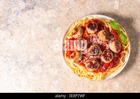 Ein Teller mit klassischen Spaghetti, garniert mit gebräunten Fleischbällchen und reichhaltiger Tomatensauce auf einem leichten Keramikgericht. Stockfoto