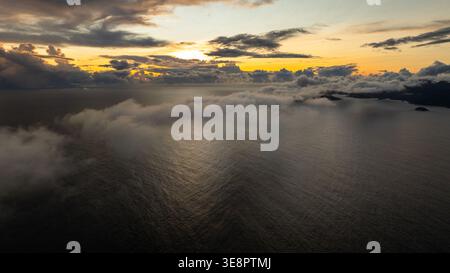Goldenes Meer mit Nebel und fernen Inseln unter einem bewölkten Himmel bei Sonnenuntergang, ruhiges Wasser. Seychellen, Mahe. Stockfoto