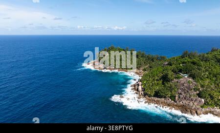 Türkisfarbenes Wasser trifft auf eine felsige Küste, umgeben von dichtem grünen Laub und malerischer Aussicht. Seychellen, Mahe. Stockfoto