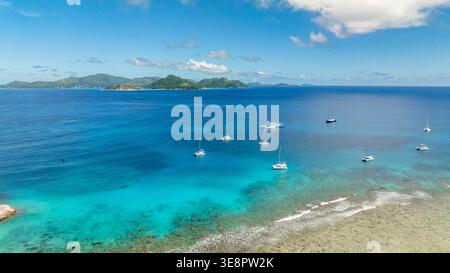 Ankerboote auf türkisfarbenem Wasser mit fernen grünen Inseln und einem klaren blauen Himmel. La Digue, Seychellen. Stockfoto