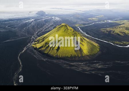 Aus der Vogelperspektive des pulsierenden, moosigen grünen Vulkans Mælifell, der aus dem krassen schwarzen vulkanischen Sand aufsteigt, im Kontrast zum fernen Gletscher Maelifell, Stockfoto
