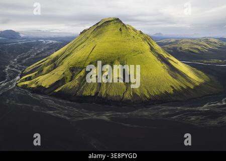 Aus der Vogelperspektive auf den lebhaften, grünen, moosigen Vulkan Mælifell, der scharf aus dem schwarzen vulkanischen Sand aufsteigt und eine surreale Landschaft schafft, Maelifell, I Stockfoto
