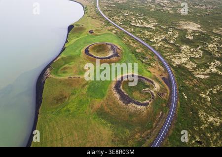 Aus der Vogelperspektive auf die gewundene Straße um Pseudokrater herum, die die lebhafte grüne Landschaft im Kontrast zur dunklen vulkanischen Erde und dem ruhigen See La verstecken Stockfoto