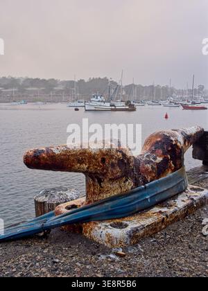 Rostiger T-Stück-Kopf-Dock-Klampe am Angelsteg, entfernter Fischtrawler, der in der nebligen Monterey Bay verankert ist Stockfoto