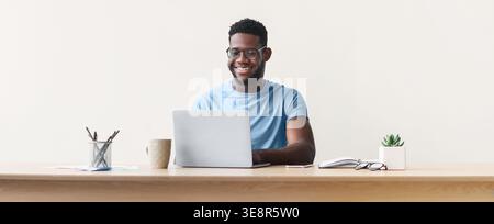 Mann, der am Laptop arbeitet, während er am Schreibtisch mit Notizbuch und Pflanze sitzt Stockfoto