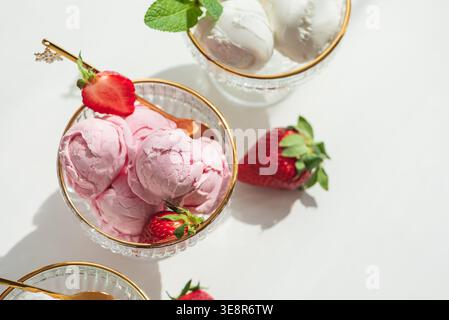 Elegante Komposition mit drei Glas-Dessertschalen mit goldenen Rändern, gefüllt mit Vanilleeis und Erdbeereis. Stockfoto