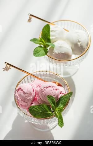Elegante Komposition mit zwei Dessertschalen aus Glas mit goldenen Rändern, gefüllt mit Vanilleeis und Erdbeereis. Stockfoto