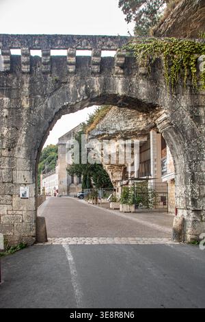Das historische, befestigte Steintor von Brantome, Frankreich, mit einem markanten Spitzbogen. Hinter dem Tor befindet sich die einzigartige Troglodyte-Fassade von Häusern Stockfoto