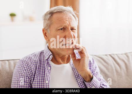 Ein älterer Mann sitzt auf der Couch und erlebt Zahnschmerzen zu Hause am Nachmittag Stockfoto